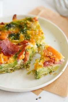 a white plate topped with a slice of broccoli and ham quiche next to a fork