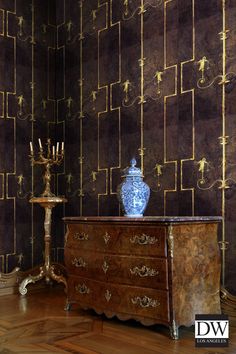 a blue vase sitting on top of a wooden dresser next to a tall golden candle holder