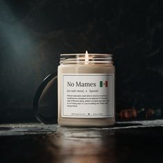 a candle sitting on top of a wooden table next to a black mug with a label that says no mames