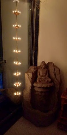 a buddha statue sitting in front of a mirror with lights hanging from it's sides