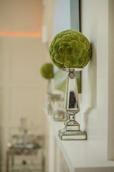 a vase filled with green flowers sitting on top of a white shelf next to a mirror