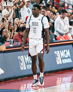 a basketball player walking on the court with fans in the stands watching from behind him