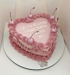 a pink heart shaped cake with cherries on the top and words written in spanish