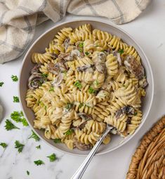 a bowl filled with pasta and mushrooms on top of a white marble table next to a wicker basket