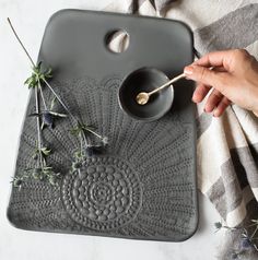 a person is holding a spoon over a tray with flowers on it and some leaves