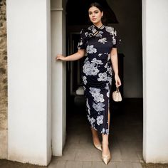 a woman in a black and white dress is standing by a doorway with her hand on the door handle