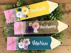 three pencils with flowers on them sitting in front of some plants and wood planks