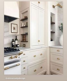 a kitchen with white cabinets and gold pulls on the doors, an oven and wine bottle