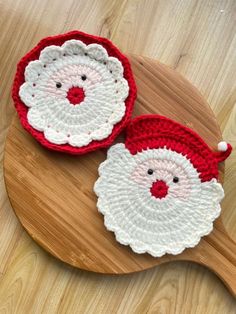 two crocheted santa claus coasters sitting on top of a wooden table next to each other