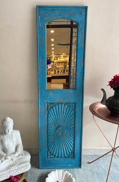 a blue door sitting next to a white statue and vase with flowers on top of it