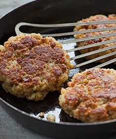 two hamburger patties being cooked in a skillet with tongs on the side