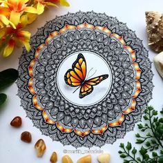 a drawing of a butterfly on a plate surrounded by rocks and flowers with the words merith, mandala written below it