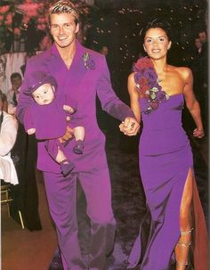 a man and woman in purple outfits walking down a runway holding hands with a baby