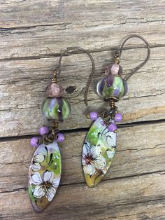 two earrings with flowers on them sitting on top of a wooden table next to each other