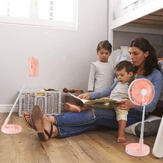 a woman sitting on the floor reading a book with two children in front of her