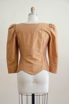 A homemade golden tan jacket, with puffed shoulders, gold faceted buttons, and good tailoring. It is unlined and light enough to be worn as a blouse. ☛ m e a s u r e m e n t s ☚ Bust: 32 Waist: 28 Shoulders: 13.5 Length: 21 ☛ d e t a i l s ☚ Era: 1990s Material: polyester Condition: excellent ☛ v i s i t t h e s h o p ☚ https://etsy.me/2Nd23kg ☛ instagram ┇ poppycockvintage ☛ facebook ┇ poppycockvintage Fitted Tops With Gold Buttons For Workwear, Fitted Gold Top For Workwear, Fitted Gold Tops For Work, Fitted Vintage Gold Blouse, Vintage Gold Fitted Blouse, Vintage Gold Blouse For Spring, Fitted Gold Vintage Blouse, Spring Vintage Gold Blouse, Vintage Fitted Tops With Gathered Sleeves