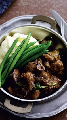 a bowl filled with meat, green beans and mashed potatoes on top of a table