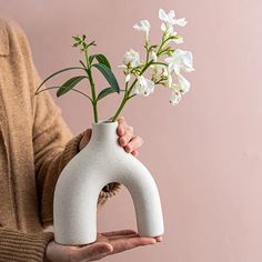 a person holding a white vase with flowers in it's palm and the inside of their hand