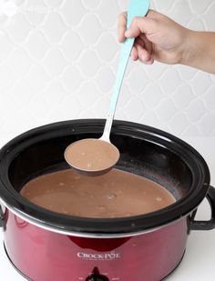 a person spooning chocolate into a crock pot with a plastic spoon in it