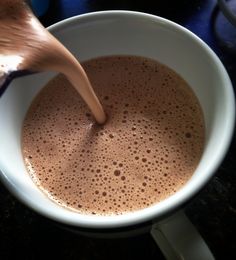 a person stirring hot chocolate in a white cup