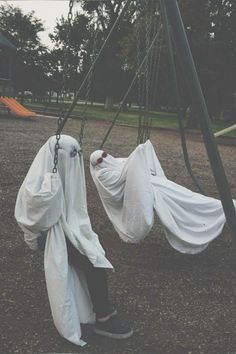 two people in white cloths are swinging on swings