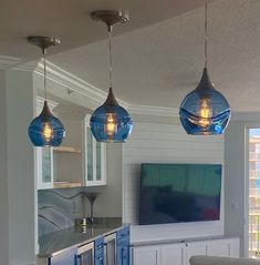 three lights hanging from the ceiling above a kitchen island with blue cabinets and drawers on it