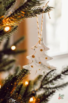 an ornament hanging from a christmas tree in front of a window with lights