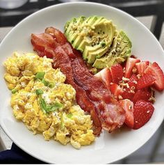 a white plate topped with eggs, bacon and avocado next to strawberries