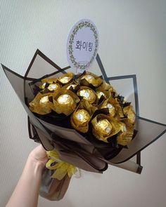 a hand holding a bouquet of chocolates wrapped in foil with a sign above it