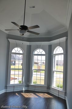 an empty room with three windows and a ceiling fan in the middle of the room