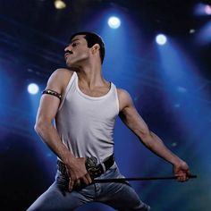 a man in white tank top holding a microphone on stage with blue lights behind him