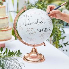 a globe with writing on it is being held by a person holding a pen and pointing to the word'the adventure begins '