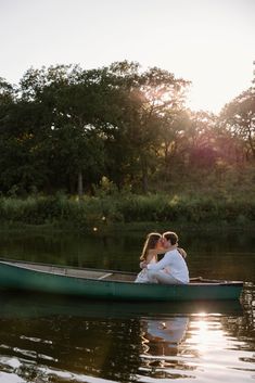 a man and woman kissing in a canoe on the water with trees in the background