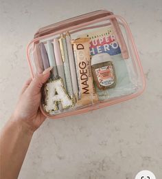 a person holding a pink case filled with writing and pencils on top of a table