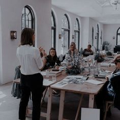 a group of people sitting around a wooden table in a room with arched windows on the walls