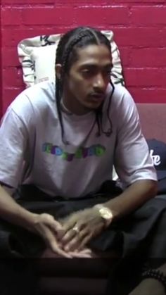 a man with dreadlocks sitting on a couch in front of a red brick wall