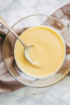 a glass bowl filled with yellow liquid on top of a white marble countertop next to a wooden spoon