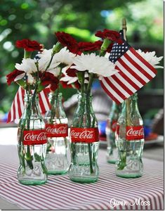 coca - cola bottles with flowers in them on a picnic tableclothed table cloth