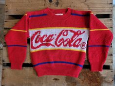 a red sweater with the word coca - cola on it hanging from a wooden pallet