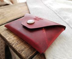 a red leather wallet sitting on top of a wooden table next to a white pillow