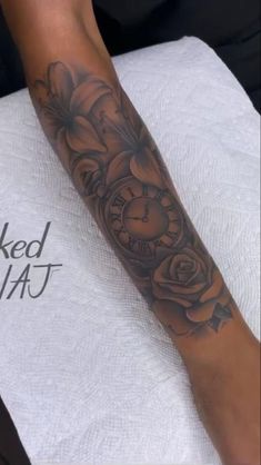 a person with a tattoo on their arm holding a clock and flowers in the background