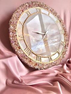 a clock with roman numerals on it sitting on a pink satin covered surface