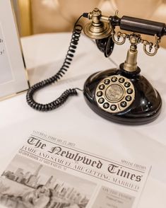 an old fashioned telephone sitting on top of a table next to a newspaper and a phone