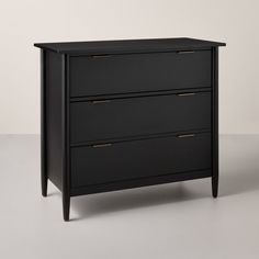 a black dresser with three drawers and gold pulls on the bottom drawer, against a white background