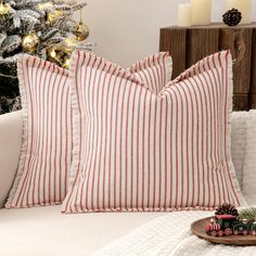 two red and white pillows sitting on top of a couch next to a christmas tree