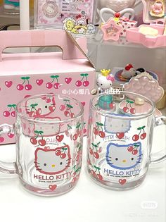 two hello kitty mugs are sitting on a table next to a box and other items