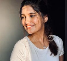 a woman smiling and wearing a white shirt with an orange lip ring on her left side