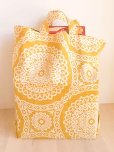 a yellow and white tote bag sitting on top of a hard wood floor next to a wall