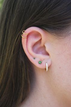 a close up of a person wearing an ear cuff with two small green stones on it