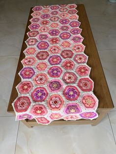 a crocheted table runner on top of a wooden table with tile flooring